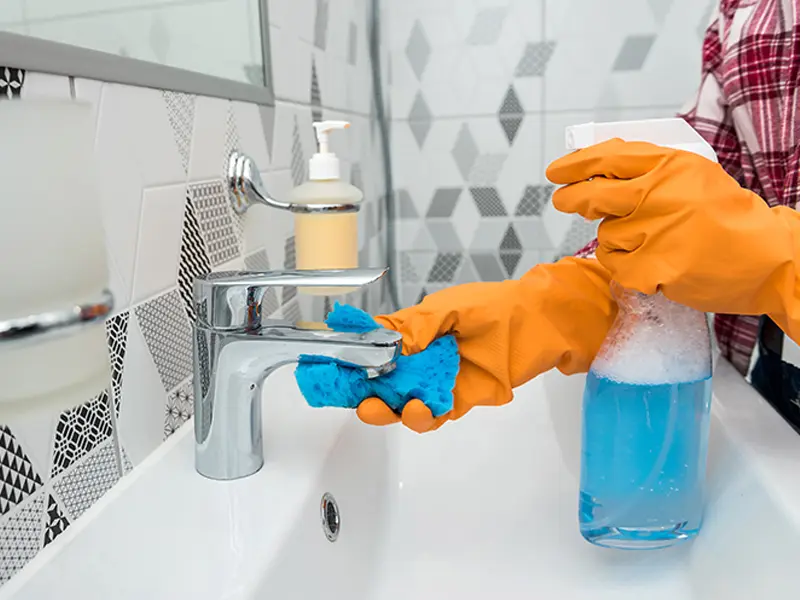 Professional cleaning a modern bathroom faucet.